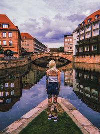 Rear view of woman walking on canal amidst buildings in city