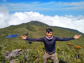 Full length of smiling young woman standing on mountain against sky