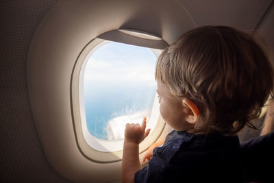 Rear view of boy looking through airplane window