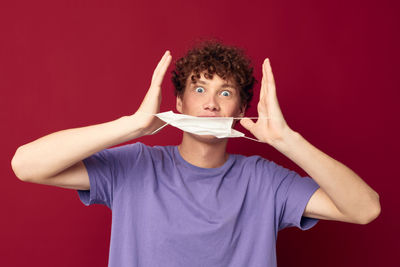 Young man holding mask against red background