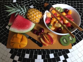 High angle view of chopped fruits with cutting board and serving tongs on floor