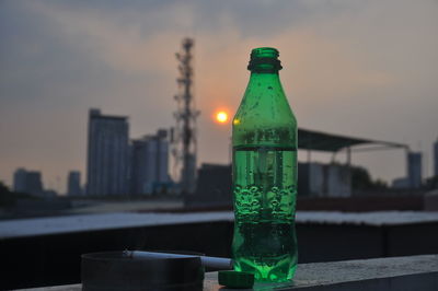 Close-up of glass bottle against sky during sunset in city