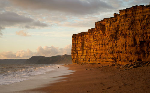 Scenic view of sea and cliffs  against sky during sunset