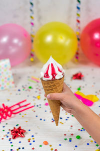 Ice cream cone in a child's hand on a birthday background with colorful decor and sweets.