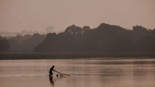 Silhouette man on boat in lake against sky