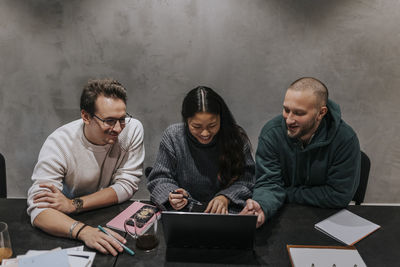 Smiling businesswoman discussing strategy over laptop with male colleagues at workplace