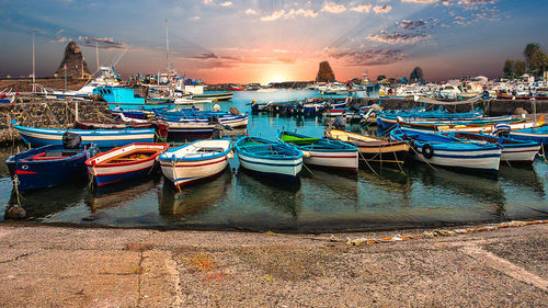 Boats moored in harbor at sunset