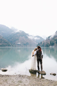 Two happy people in love the bride and groom in wedding outfits embrace by the lake and mountains