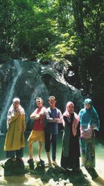 Full length of friends standing by waterfall in forest