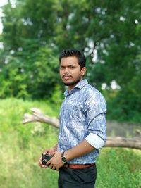 Young man using phone while standing against trees