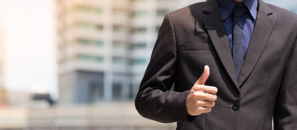 Midsection of businessman showing thumbs up in city