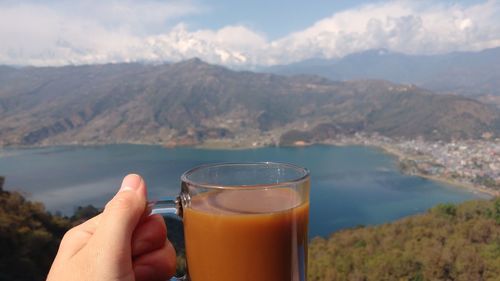 Close-up of hand holding drink against lake