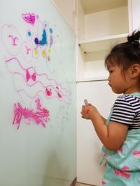 Cute girl drawing on transparent wipe board at home