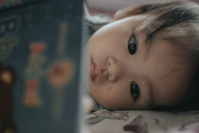 Close-up of cute baby girl resting on bed