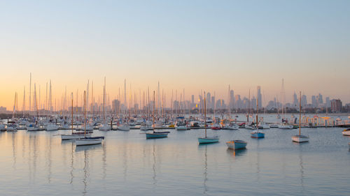 Sailboats moored in harbor against clear sky during sunset