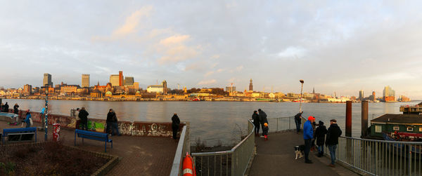 People on city buildings by sea against sky