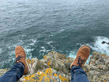 Low section of man sitting on rock by sea