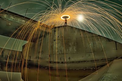 Low angle view of man spinning illuminated lighting equipment at night