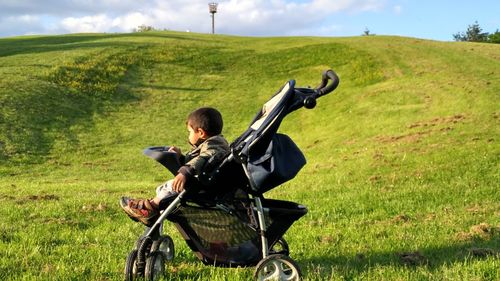 Side view of boy sitting in stroller at field