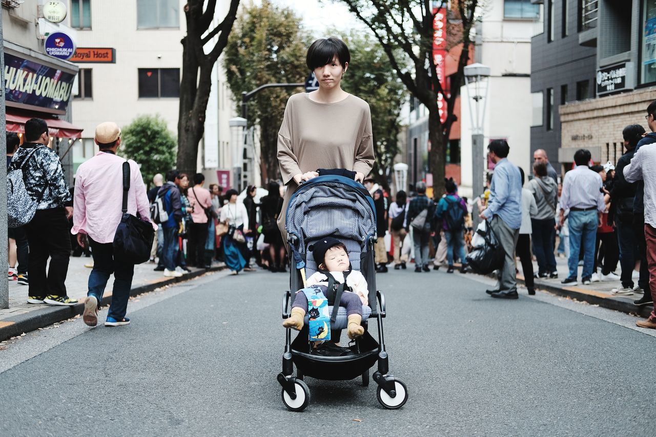 city, group of people, architecture, building exterior, real people, street, casual clothing, transportation, built structure, day, full length, lifestyles, men, large group of people, focus on foreground, women, child, leisure activity, road, outdoors