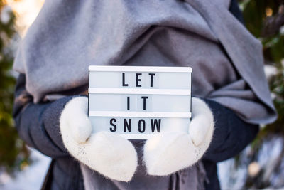 Midsection of person wearing warm clothing holding message during winter