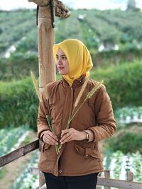Portrait of young woman standing against fence