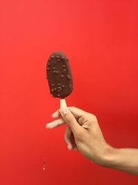 Cropped image of person holding ice cream against red background