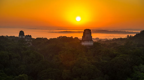 Built structure by trees against orange sky