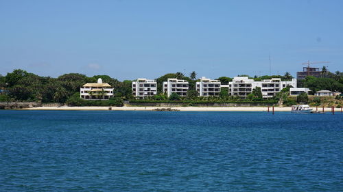 Buildings by sea against clear blue sky