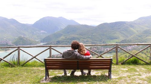 Rear view of couple sitting on bench while looking at mountains