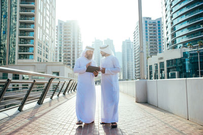 Male coworkers discussing over digital tablet while standing on footbridge in city