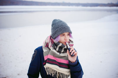 Woman smoking electronic cigarette while standing on snow covered landscape against sky