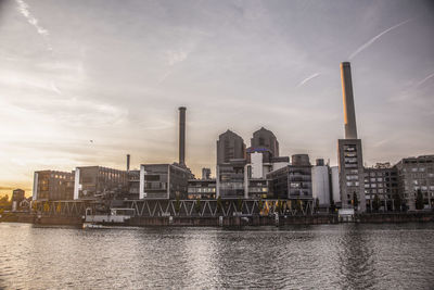 Buildings by river against sky in city during sunset