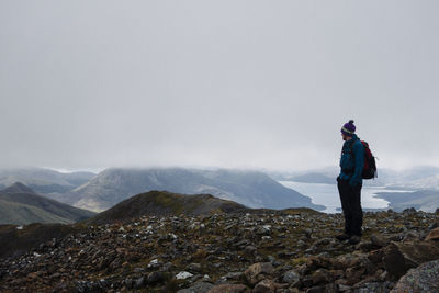 Rear view of man standing on rock against sky