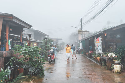 People walking on wet road in city during rainy season