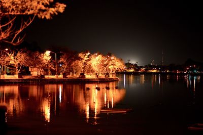 Illuminated city by lake against sky at night