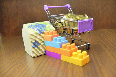 Close-up of coins in shopping cart with house model and toy blocks on wooden table