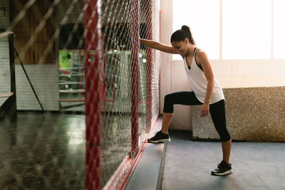 Full length of woman standing by fence in gym