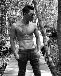 Shirtless young man standing on boardwalk against trees in forest