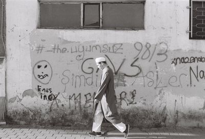 Side view of man walking on footpath by wall