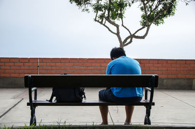 Rear view of man sitting on bench against the wall