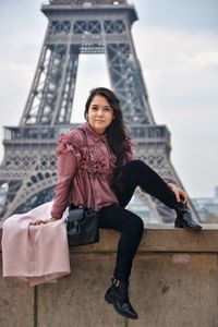 Portrait of smiling woman sitting on wall against eiffel tower