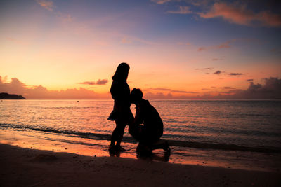 Silhouette boyfriend kissing pregnant girlfriend abdomen at beach