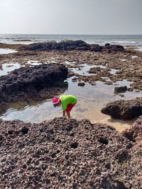 Man on rock at beach against sky