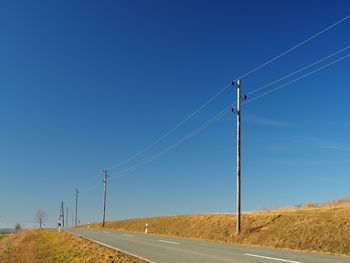 Electricity pylons on road against clear blue sky
