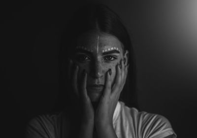 Close-up portrait of young woman with make-up against black background