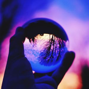 Close-up of hand holding crystal ball against sky