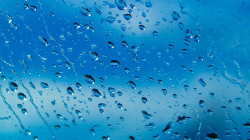 Full frame shot of wet glass window showing water droplets on sky background 