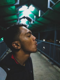 Close-up profile view of young man emitting smoke while standing on elevated walkway