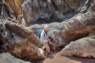 Man with camera walking amidst rock formation